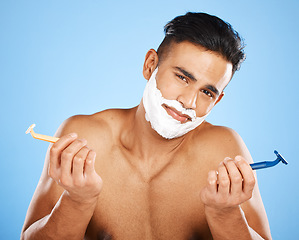 Image showing Razor, choice and portrait of man with shaving cream making decision to shave beard in studio. Clean, hygiene and guy from India with doubt and shavers to groom face hair isolated by blue background.