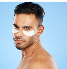 Image showing Eye patches, skincare and portrait of man standing in studio doing a cosmetic beauty routine. Self care, healthy and male model doing face treatment with a facial product isolated by blue background.