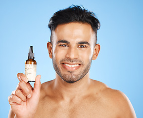 Image showing Indian man, serum and skincare with smile for natural beauty, organic facial and wellness with blue studio background. Body care, male and with cosmetic oil for smooth skin, glow and happy to hydrate