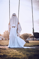 Image showing Halloween, costume and ghost couple at park, kid enjoy scary holiday with parent. Family, festival and child with mom or dad in spooky white sheet dress up with sunglasses sitting on playground swing