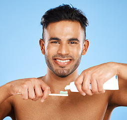 Image showing Mouth, dental and man brushing teeth in studio for wellness, health and grooming on blue background. Portrait, face and teeth of indian guy happy with oral cleaning product, toothpaste and mockup