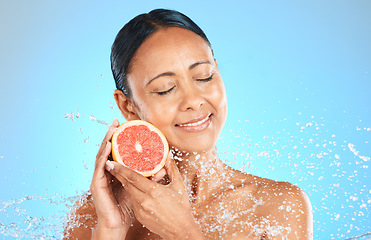 Image showing Skincare, beauty and woman with grapefruit in studio for cleaning, grooming and wellness against blue background. Face, water and fruit product with girl skin model relax, smile and facial, treatment