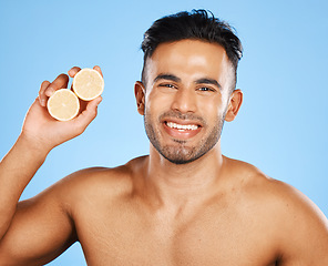 Image showing Face, skincare and orange with a man model in studio on a blue background to promote natural beauty. Portrait, fruit and wellness with a handsome young male posing for a health product or treatment