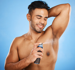 Image showing Deodorant, beauty and grooming with a man model using antiperspirant in studio on a blue background. Body spray, aerosol and smell with a handsome young male spraying a scent product to his underarm