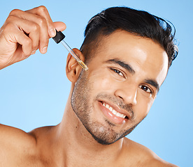 Image showing Man face, skin serum or beard oil of facial hair growth beauty product on blue studio background. Portrait of a happy young arab guy model, liquid dermatology and hyaluronic acid for body cosmetics