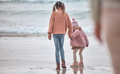 Image showing Children, ocean and holding hands sisters standing on sea sand, relax and watching waves together on vacation. Freedom, fun and young girl with toddler hold hands and play on beach on summer holiday.