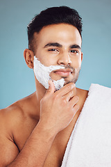 Image showing Face, beauty and shave with a man model in studio on a blue background for shaving or grooming. Portrait, skincare and hair removal with a handsome young male shaving his beard in the bathroom