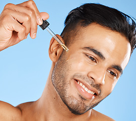 Image showing Oil, skincare and man with serum for face against a blue studio background. Wellness, happy and young model with a liquid with hyaluronic acid for growth of beard, cleaning and dermatology health