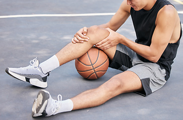 Image showing Basketball, man and knee in sports injury on the court holding painful, sore or tender area in the outdoors. Basketball player suffering from leg pain, joint or inflammation in sport match or game