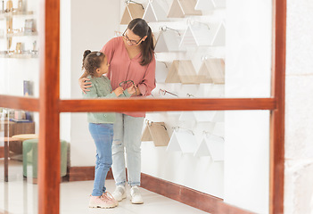 Image showing Mother, girl and shopping, glasses and optometrist for lense, frame and vision together in retail store. Woman customer buy prescription with child for eyesight in optometry shop to choose or choice