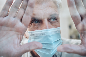 Image showing Hands, covid and quarantine with a senior man in a mask standing behind glass in a house during lockdown. Window, sad and isolated with a mature male in a retirement home during corona virus pandemic