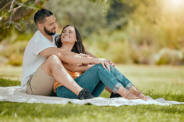 Image showing Couple relax on grass, outdoor picnic in park and love sitting on blanket in Miami garden under a tree. Romantic date in spring, woman smile at happy boyfriend or summer holiday together in sunshine