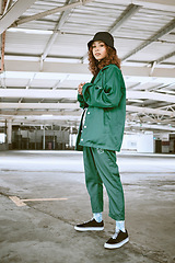 Image showing Portrait, fashion or stylish young gen z woman stand in a warehouse with green clothing. Trendy, hipster latino girl with attitude and curly hair in industrial building or factory with pride or cool