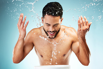 Image showing Studio, water splash and face skincare of man isolated against a blue background. Health, hygiene and male model washing face, cleaning and grooming routine for wellness, beauty or facial freshness.