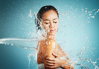 Image showing Water, splash and hygiene with a woman washing or cleaning in studio on a blue background. Bathroom, cleansing and skincare with an attractive young female wet in the bathroom for body hydration