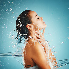 Image showing Water, hydration and cleansing with a woman in studio on a blue background with a liquid splash for hygiene. Relax, luxury and wellness with an attractive young female washing in a bathroom or shower