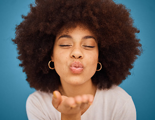 Image showing Care, love and black woman blowing kiss with a smile, afro hair and hand against a blue studio background. Happy, beauty and face of a cool, African and young girl model with affection and happiness