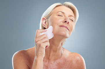 Image showing Face, beauty and massage with a senior woman in studio on a gray background for skincare to relax. Skin, wellness and antiaging with a mature female using a massaging tool for natural treatment