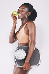 Image showing Happy woman, scale and apple for losing weight, healthy diet and fitness results, progress and exercise motivation on studio background. Black model eating fruits, sports nutrition and body wellness