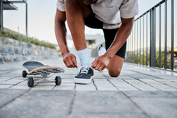 Image showing Black man, shoes and skateboard, skater with shoelace in urban skate park for fitness, exercise and fun outdoor. Young person, cool and trendy out in nature, skating with sneakers and cityscape.
