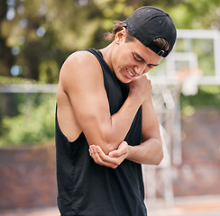 Image showing Sport injury, basketball and man in pain while playing on basketball court, fitness and hurt elbow outdoor. Young athlete holding arm, sore and exercise accident, sports and training in park.