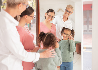 Image showing Mirror, glasses and girl with mother and optometrist at optometry shop shopping or trying new spectacles. Smile, vision and happy kid looking at reflection testing eyewear or lenses at optics store.