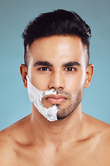 Image showing Portrait, skincare and man shaving in studio on blue background for facial hair grooming in India. Healthy, products and young face model shaves beard and mustache in self care routine with cream