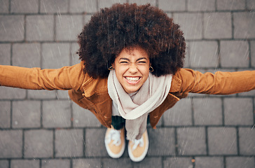 Image showing Black woman, stand to feel rain and happy in city in winter with smile, afro or trendy fashion. Woman, outdoor above or happiness in drizzle, splash and face in metro, urban or town with natural hair