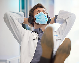 Image showing Doctor, covid face mask and relax in healthcare hospital with headphones to listen to music after finished task, job or pandemic. Medical worker man at work during covid 19 for safety and care