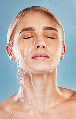 Image showing Water, skincare and face of a woman with a splash for cleaning, treatment and care against a blue studio background. Wellness, health and girl model with luxury facial dermatology to relax for beauty