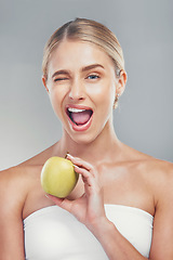 Image showing Woman, health and wink portrait with apple for fiber diet, nutrition and wellness lifestyle. Fruit, healthy and digestion dieting marketing with happy model girl on gray studio background.