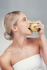 Image showing Nutrition, smile and woman eating an apple for health of teeth, dental and care for body against a grey studio background. Food, diet and happy model thinking of healthy lifestyle with a fruit