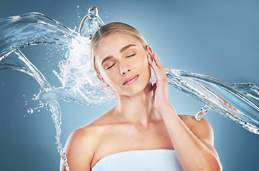 Image showing Face, beauty and water splash of woman with eyes closed isolated on a blue background in studio. Skincare hygiene, facial cleaning and young female model from Canada feeling refreshed and healthy.