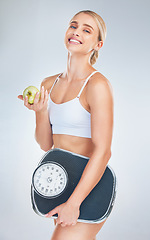 Image showing Health, lose weight and woman with an apple and scale for body goal, motivation and nutrition against a grey studio background. Food, happy and portrait of athlete model with smile for fruit and diet