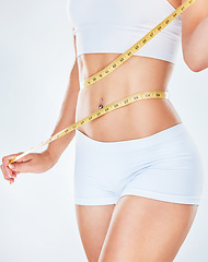 Image showing Body, tape measure and diet with a woman measuring her waist to track weightloss in studio on a gray background. Fitness, health and wellness with a young female mentoring her diet for losing weight