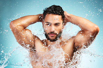 Image showing Water, splash and man washing his body on a blue studio background for health and wellness. Bodycare, hygiene and man cleaning or cleansing his body for beauty, wash and clean fresh routine