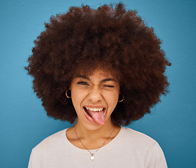 Image showing Face, portrait and woman with tongue out being silly and goofy on a blue studio background. Amusing, comic and crazy african american female making a funny, humour face on a backdrop