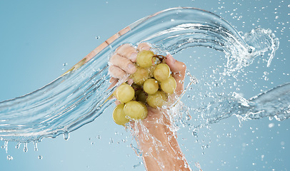 Image showing Hands with grapes, water splash and studio blue background of fruits sustainability, healthy lifestyle and juice detox, nutrition and vitamins. Bunch of clean, vegan and diet green grapes in wet palm