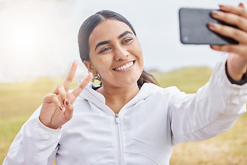 Image showing Woman runner, phone selfie and peace sign in nature, park or grass for social media after exercise. Girl, smartphone and smile in photo outdoor at training, running or workout in morning for web blog