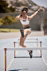 Image showing Fitness, hurdles and athlete jumping on track at an outdoor stadium for cardio workout. Sports, running and woman doing athletics on field for training and exercise with energy, motivation and speed.