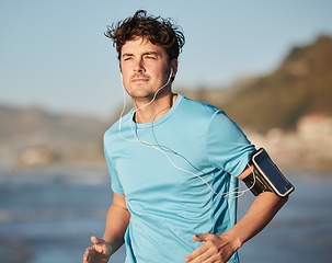 Image showing Running, music and man athlete at beach with headphones run by the ocean with audio streaming. Mobile radio, web podcast or training song of a runner athlete listening to a track on an outdoor run