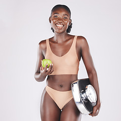 Image showing Black woman, scale and apple to lose weight, healthy diet and fitness results, progress and exercise motivation isolated on studio background. Happy model eating fruit, nutrition and body wellness