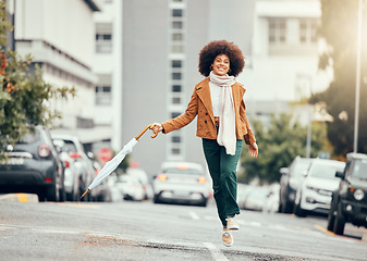 Image showing Black woman, umbrella and jump on street, city or road outdoors. Happy, smile and carefree female from South Africa skipping on pavement in urban town, traveling or having fun time alone on sunny day