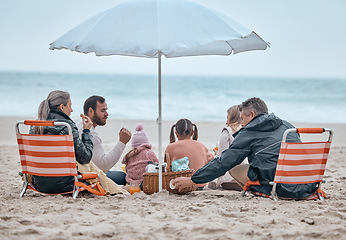 Image showing Family, beach food and relax on holiday, vacation or trip outdoors on sandy seashore. Back view, bonding and grandparents and mom, dad and kids enjoying quality time together under beach umbrella.