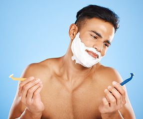 Image showing Man, razor and shaving in studio for choice, confused or thinking of skin, cosmetics or performance. Model, shaving cream or blade for shave, grooming or skincare for hair on face by blue background