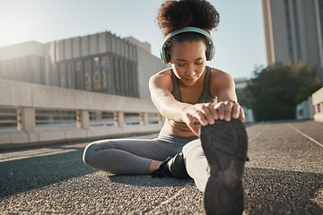 Image showing Stretching, foot and city black woman on floor with headphones, sneakers and training gear for outdoor running, exercise and workout. Sports, fitness and girl listening to music for muscle warmup