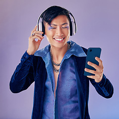 Image showing Headphones, studio and gay man with makeup listening to music on the internet with smartphone. Cosmetics, lgbtq and happy guy streaming audio, podcast or radio on phone isolated by purple background.