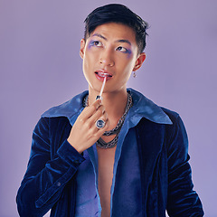 Image showing Beauty, makeup and lgbt Asian man in studio on purple background using cosmetics, beauty products and lipstick. Creative, fashion and queer or lgbtq male model with lip gloss, eyeshadow and style