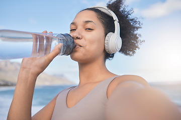Image showing Woman runner, drinking water and selfie with music while outdoor for exercise, workout or fitness. Black woman, headphones and beach for training, wellness or health in nature by ocean in summer sun
