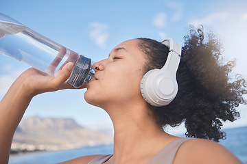 Image showing Fitness, headphone and woman drinking water after running, training and cardio workout at beach. Exercise, runner and thirsty with healthy liquid for hydrate, energy and wellness listening to music